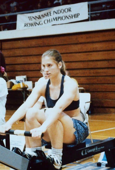A UTC rower on a Concept2 ergometer under the Tennessee Indoor Rowing Championship banner at Maclellan Gymnasium, 1996–97.