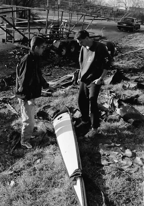 Two UTC Rowing athletes examining a charred shell fragment in the grass next to the burnt trailer.