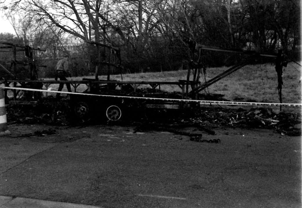 The burnt trailer surrounded by yellow police 'NO PARKING' tape, with an investigator visible.