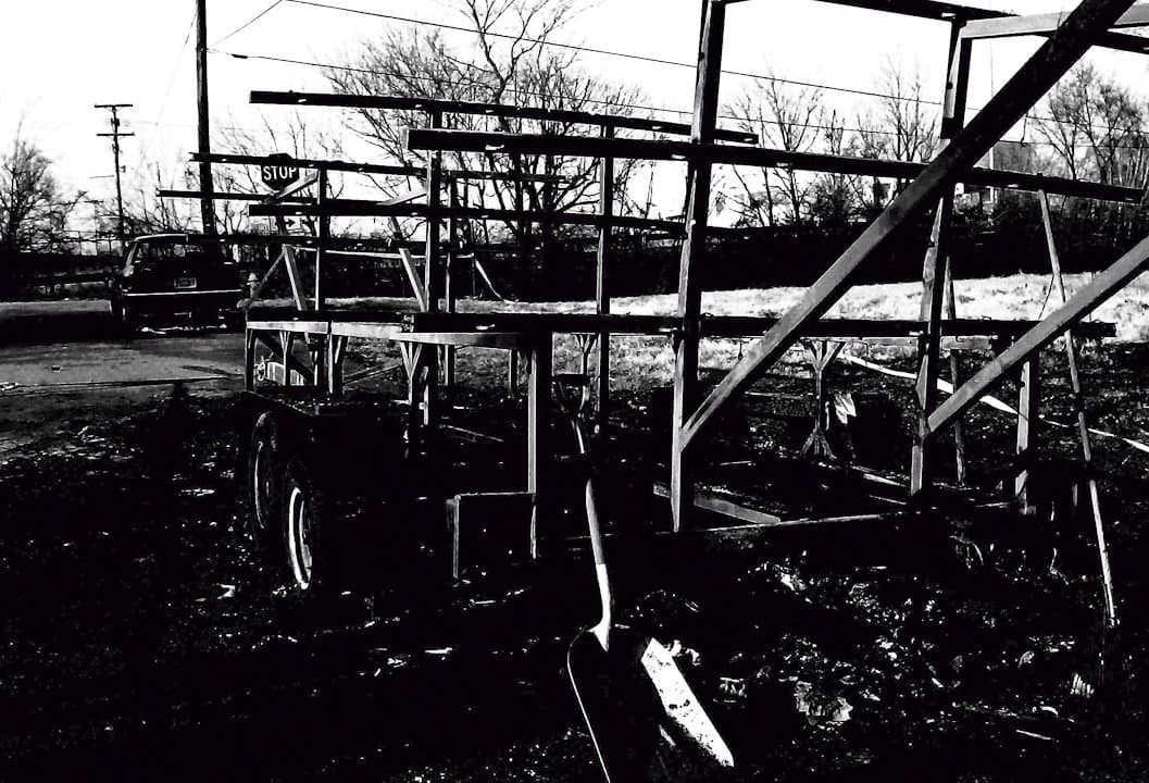 Wide view of the salvage operation: five or more UTC athletes working among shell pieces in a winter field, with the boathouse structure visible in the background.