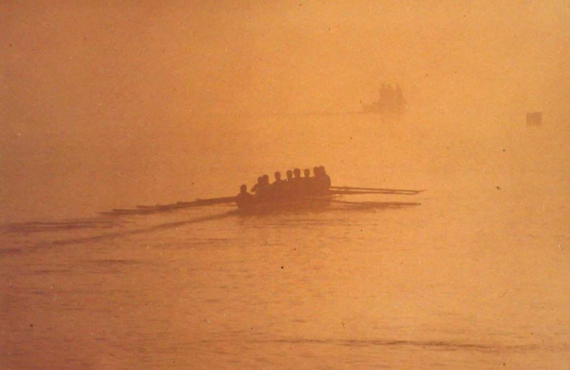 Silhouetted UTC men's eight rowing through fog at sunrise on the Tennessee River, mid-1990s.