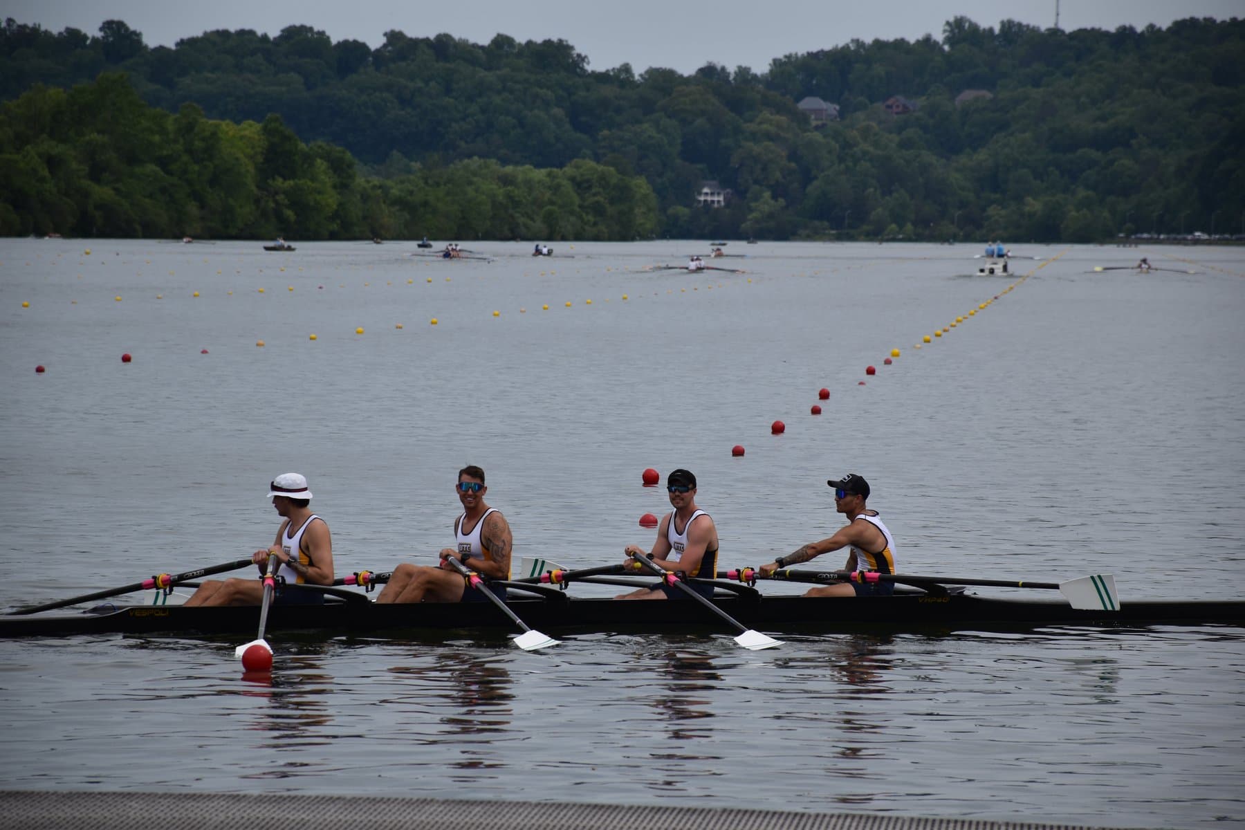UTC Rowing's M4x in the water at ACRA Nationals, Melton Hill Lake, Oak Ridge TN — all four rowers (Mako, Richardson, Burkett, Pollard) seated in the boat, side profile, lane buoys visible.
