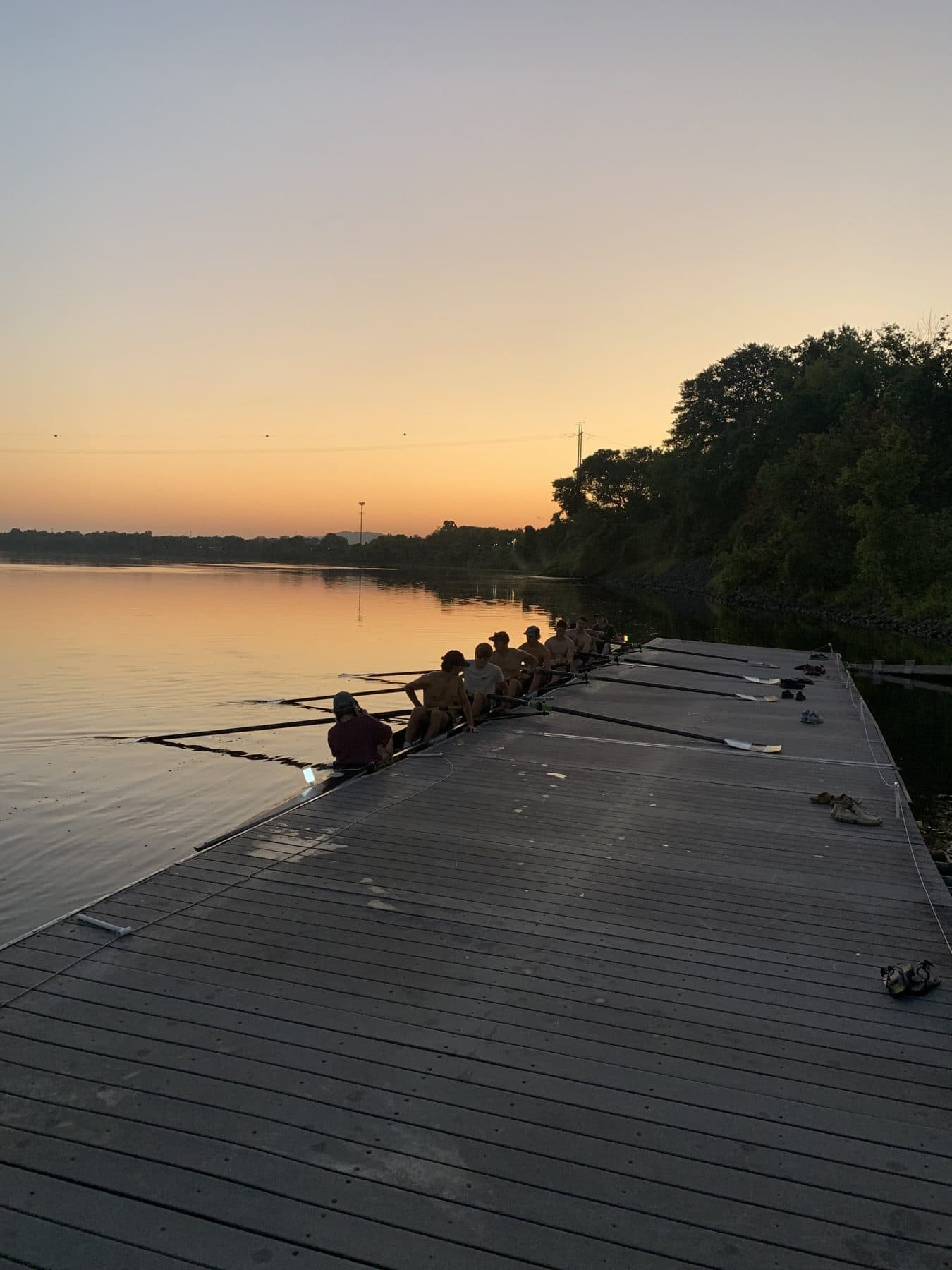 A UTC eight sitting at the dock at dawn, rowers in the boat, the Tennessee River glowing orange.