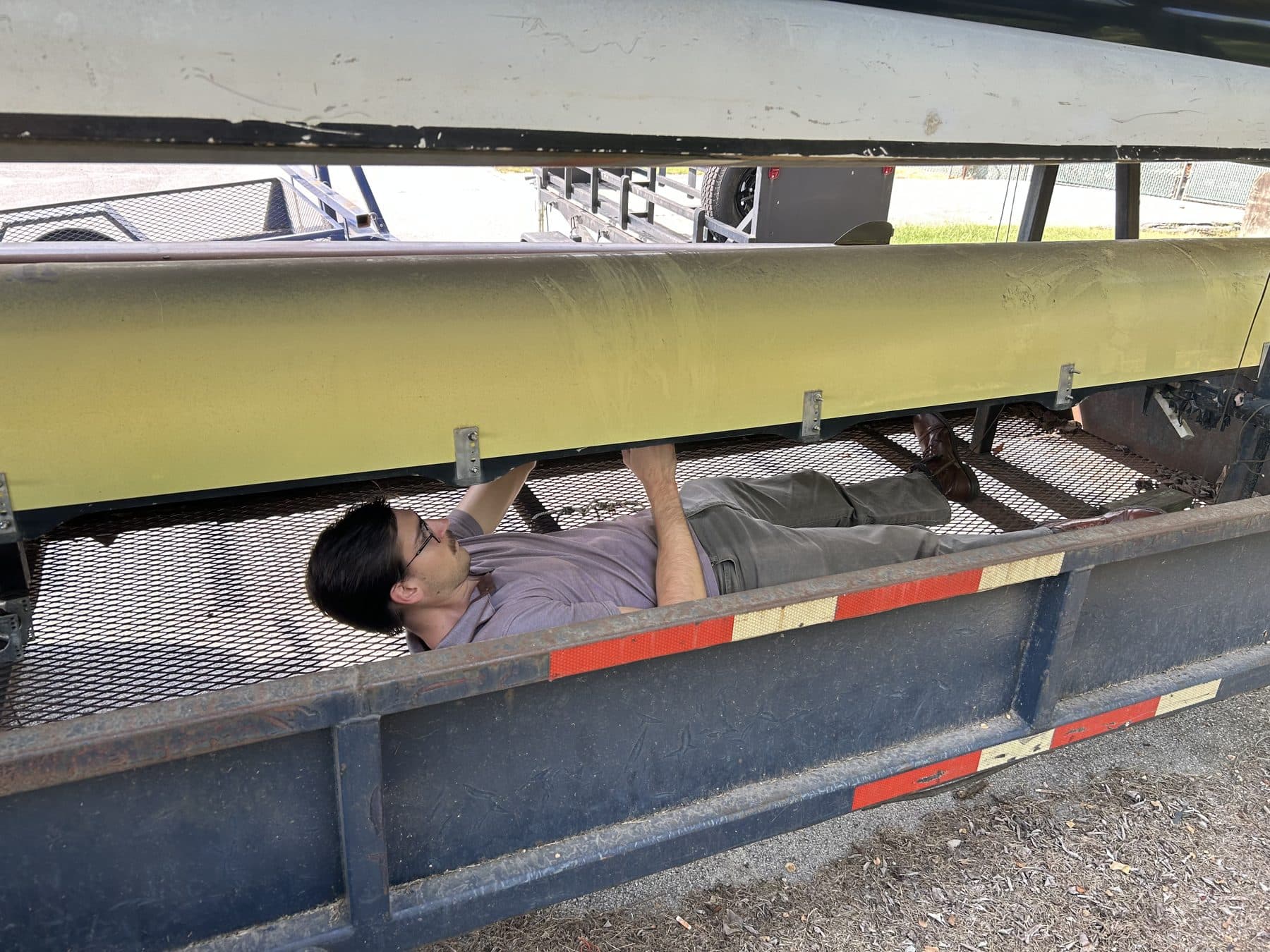 A UTC rower lying under a shell on the boat trailer, working on repairs.