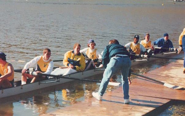 Men's 8+ launching at a dock — eight rowers in yellow/black UTC kit, coach assisting at bow