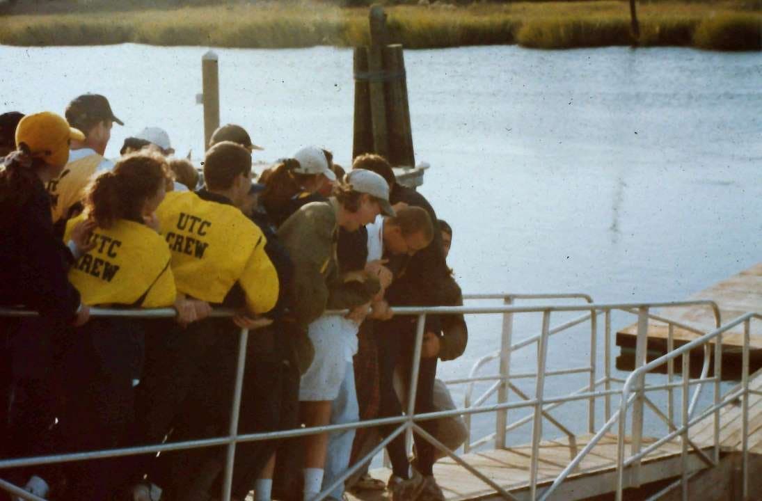 UTC CREW jackets and a crowd of athletes on a dock railing, watching/managing a launch